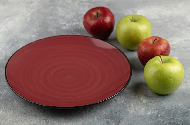 Prato vermelho vazio com maçãs vermelhas e verdes na mesa de pedra.