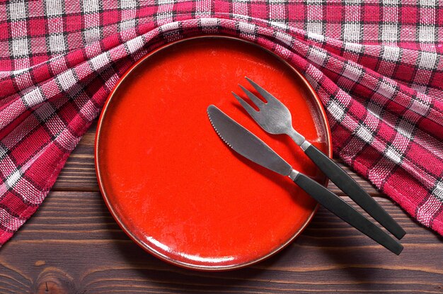 Prato vermelho vazio e talheres na vista superior da mesa de madeira escura