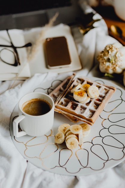 Prato, waffle pequeno almoço, com, banana, topping, ligado, um, branca, cama, perto, um, diário, e, um, telefone