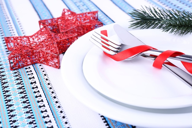 Pratos brancos, faca, garfo, guardanapo e decoração de Natal na toalha de mesa