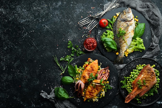 Pratos de frutos do mar Peixe dourado robalo e lula Em um fundo de pedra preta Vista superior Espaço para cópia gratuita