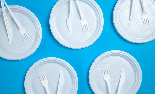 Pratos de plástico branco garfos e facas sobre fundo azul