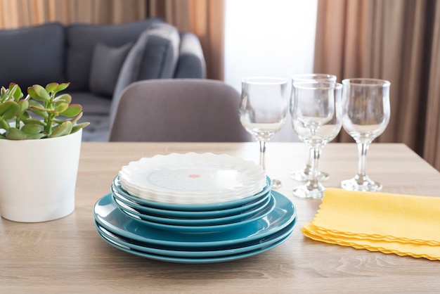 Pratos limpos em cima da mesa. placas azuis e brancas limpas empilhadas, vidros e guardanapos amarelos na tabela de madeira na cozinha.