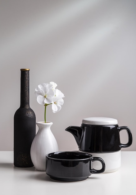 Pratos preto e branco e uma flor em um vaso sobre um fundo claro.