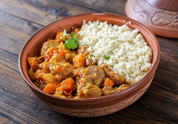 Pratos tradicionais tajine, cuscuz e salada fresca na mesa de madeira rústica.