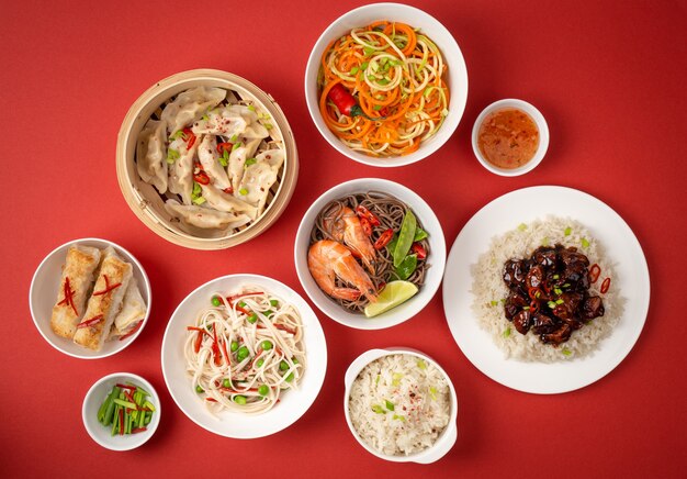 Pratos variados da cozinha tradicional chinesa em fundo vermelho: frango agridoce com arroz, bolinhos no vapor de bambu, pãezinhos fritos, macarrão com camarão. Conceito de comida asiática, vista de cima