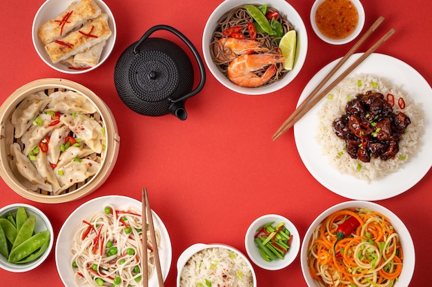 Foto pratos variados da cozinha tradicional chinesa em fundo vermelho: frango agridoce com arroz, bolinhos, pãezinhos fritos, macarrão e chaleira. conceito de comida asiática, vista de cima, espaço para texto