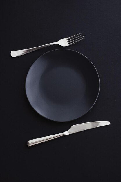 Pratos vazios e talheres em talheres premium de fundo preto para dieta e design minimalista de jantar de férias