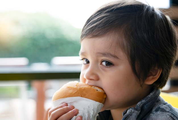 Pré-escolar garoto comendo hambúrguer sentado no café