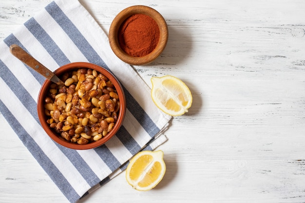 Prebranac Frijoles al horno de los Balcanes. Cocina serbia, montenegrina, bosnia, croata, eslovena. Frijoles crudos, cebolla, limón, pimentón en polvo. Fondo de madera blanca Vista superior. Espacio para texto