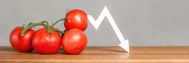 El precio de los tomates y las verduras Mala cosecha de verduras Tomates maduros rojos frescos con ramitas sobre la mesa El gráfico apunta hacia abajo