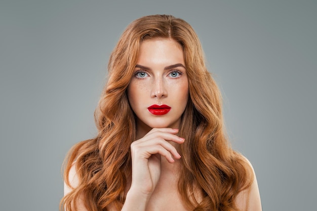Preciosa modelo con el pelo rojo largo y rizado mirando a la cámara. Cabello ondulado brillante, cara perfecta.