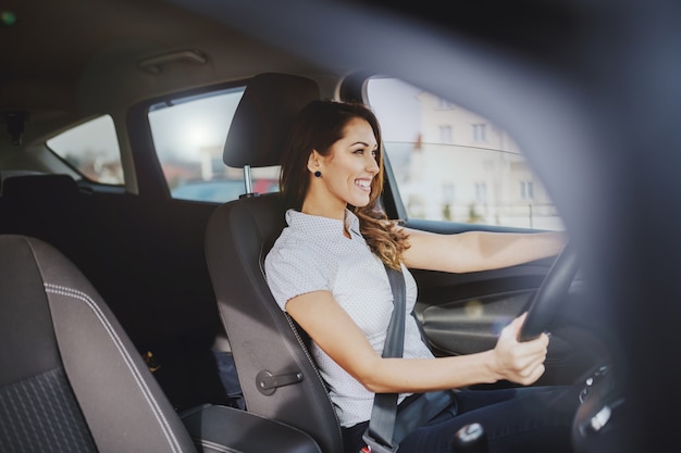 Preciosa morena caucásica sonriente conduciendo su coche.