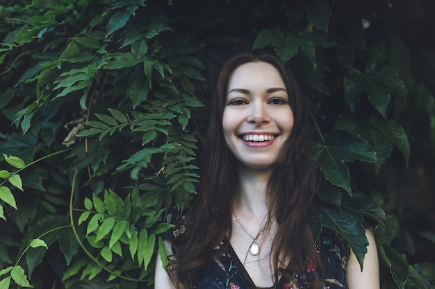 Preciosa morena en un follaje verde, sonriendo.