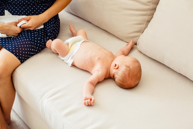 Precioso bebé recién nacido acostado en el sofá cerca de las rodillas de la madre después de cambiarse de ropa