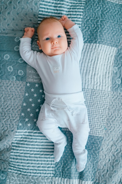 Precioso bebé recién nacido con ojos azules acostado en la cama.