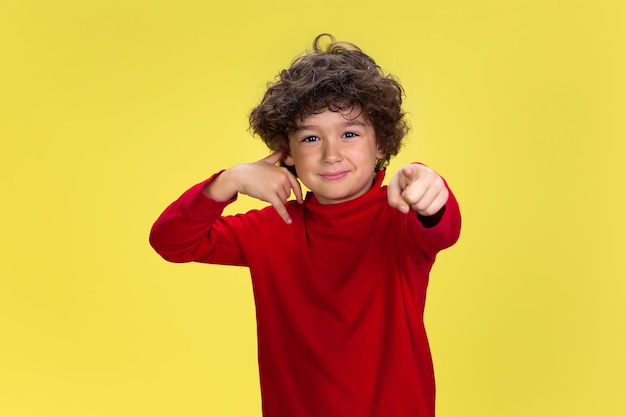 Preciso que você ligue Retrato de menino encaracolado bonito com roupa vermelha no fundo amarelo do estúdio Conceito de educação de expressão infantil Pré-escolar com expressão facial brilhante e emoções sinceras