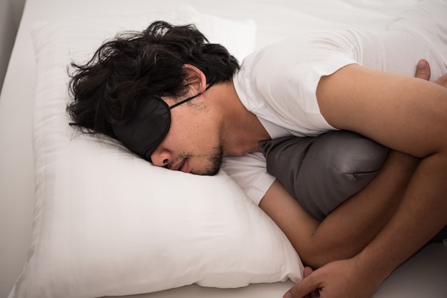 Preguiça do homem asiático que ainda está dormindo na cama no quarto da manhã, hora de acordar