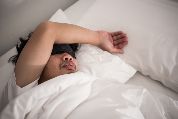 Preguiça do homem asiático que ainda está dormindo na cama no quarto na manhã