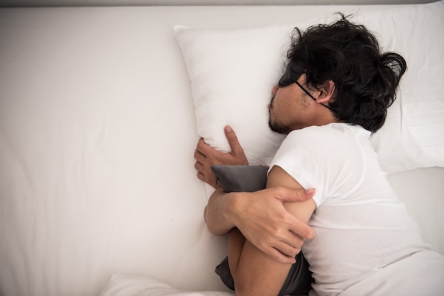 Preguiça do homem asiático que ainda está dormindo na cama no quarto na manhã