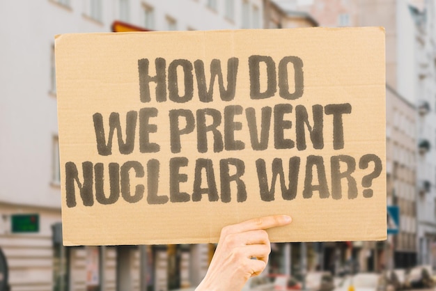 La pregunta ¿Cómo podemos prevenir la guerra nuclear? está dibujada en una pancarta de cartón en las manos de los hombres Conflicto Crisis Amenaza Misil Bomba Explosión Destrucción Devastación Radiación Fallout Defensa