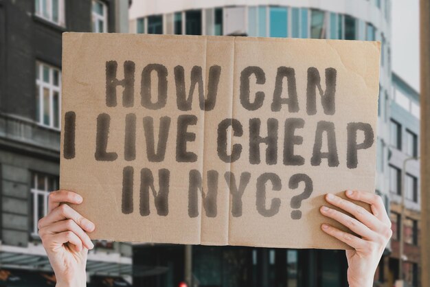 La pregunta ¿Cómo puedo vivir barato en la ciudad de Nueva York? está en una pancarta en manos de hombres con un fondo borroso Elección Gastos Economía Vivir Estado financiero Aumento económico Tasa de dinero de Nueva York