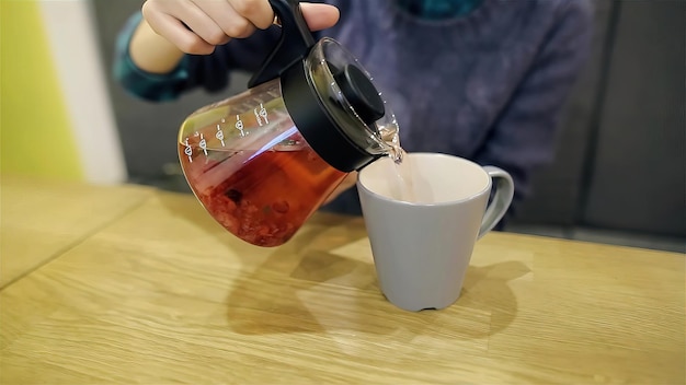 Prejudicando as mãos de uma jovem derramando chá escandinavo quente com mirtilos e hortelã em uma xícara grande Closeup