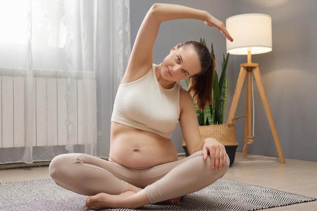 Prenatale Übungen Prenatale Fitness Yoga Gesunde Schwangerschaftspflege Übung für werdende Mütter Schöne schwangere Frau trainiert, während sie in der Lotusposition sitzt und ihren Körper dehnt