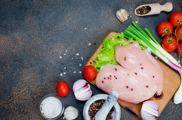 Prendedero crudo del pollo en tabla de cortar con las especias y las hierbas.