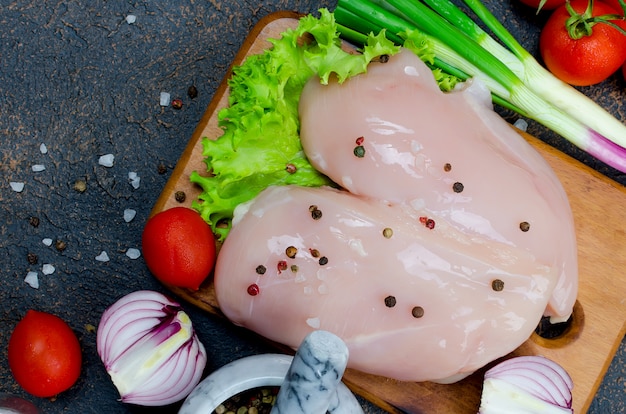 Prendedero crudo del pollo en tabla de cortar con las especias y las hierbas.