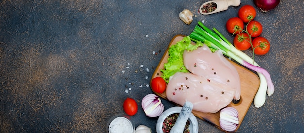 Prendedero crudo del pollo en tabla de cortar con las especias y las hierbas.