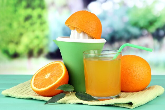 Prensa de cítricos vaso de jugo y naranjas maduras sobre mesa de madera verde