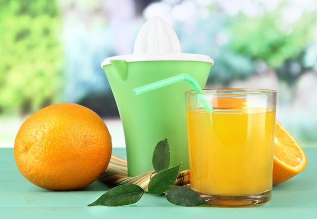 Foto prensa de cítricos vaso de jugo y naranjas maduras sobre mesa de madera verde