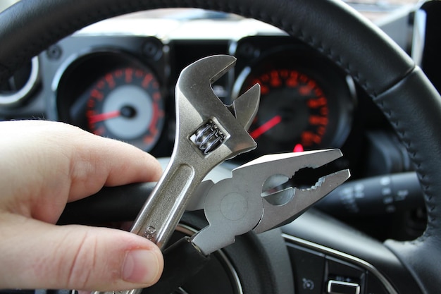 Prensas e chave ajustavel em dedos humanos em frente ao painel de carro desfocado com dígitos vermelhos