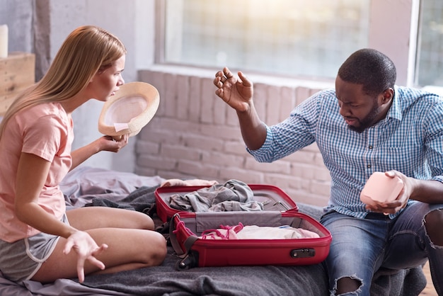 Preocupación y pánico. Joven pareja dulce internacional discutiendo mientras se prepara para tener vacaciones juntos