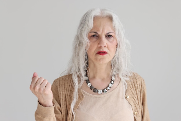 Preocupada anciana con largo cabello gris rizado suelto se encuentra sobre fondo blanco dama madura