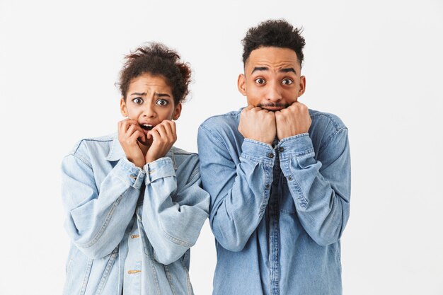 Preocupada pareja africana cubriendo sus bocas mientras sobre pared gris