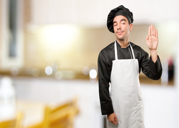 Preocupado joven chef haciendo un gesto de prohibición