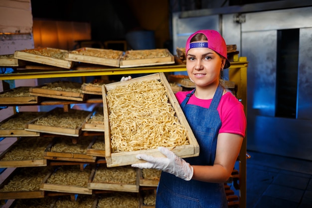 Prepara los fideos. Fábrica de pasta. Producción de espaguetis. Pastas crudas. Trabajador con una caja de pasta. Chica trabaja en la producción de pasta.