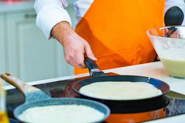 Preparação da cozinha: o chef frita panquecas frescas em duas panelas