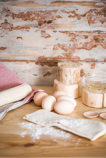 Preparação da massa. Ingredientes para a massa - ovos e farinha com um rolo. No fundo de madeira