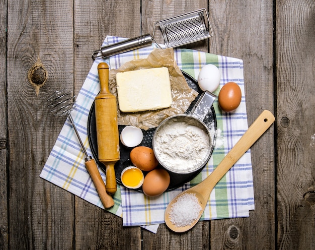 Preparação da massa. Ingredientes para a massa - ovos, manteiga, farinha, sal e ferramentas no tecido. Sobre superfície de madeira. Vista do topo