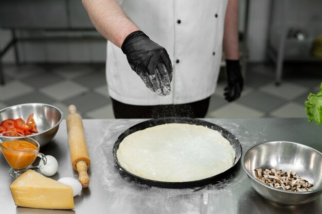 Preparação da massa para pizza closeup da mão do cozinheiro polvilhando a massa com farinha