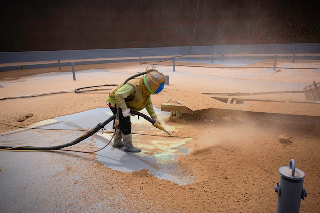 Preparação da placa de corrosão da superfície do trabalhador masculino por jateamento de areia no convés superior do tanque