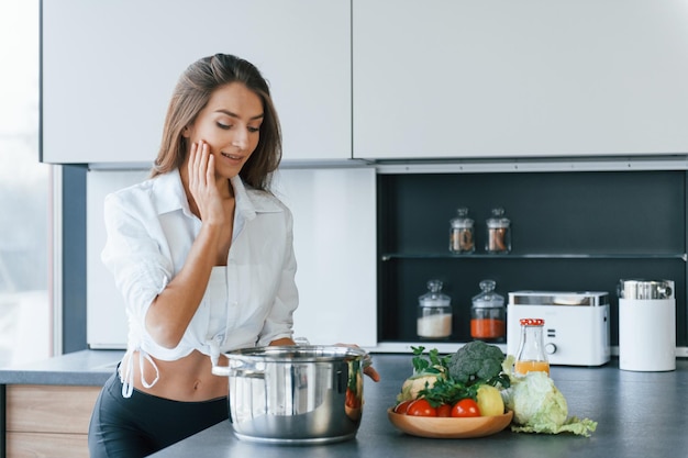 Preparação da refeição na tigela A jovem europeia está dentro de casa na cozinha dentro de casa com comida saudável