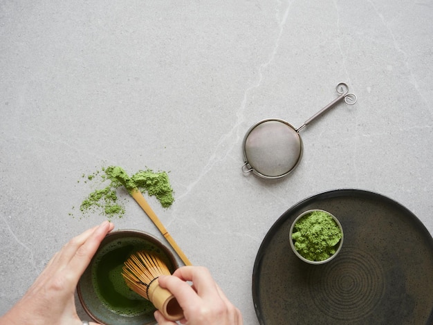 Preparação de bebida de chá verde com pó de matcha Mãos com batedor de bambu tradicional sobre a tigela