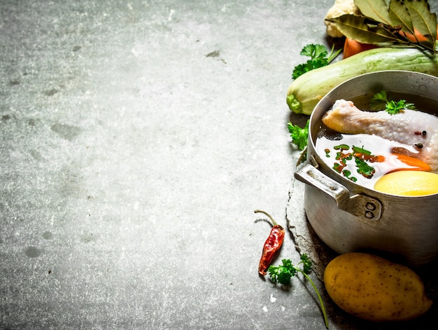 Preparação de canja de galinha perfumada com legumes frescos. Na mesa de pedra.