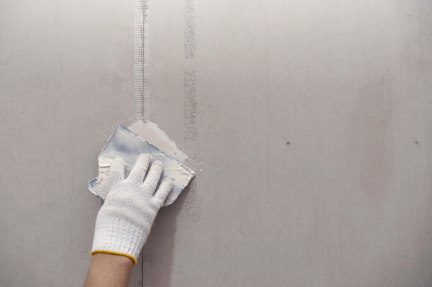 Preparação de gesso e pintura de parede fecha a mão do artesão aplicando remendo de drywall de enchimento