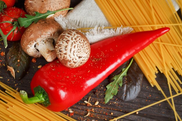 Preparação de macarrão espaguete com tomate, alho, cogumelos, pimenta e azeite, na mesa de madeira