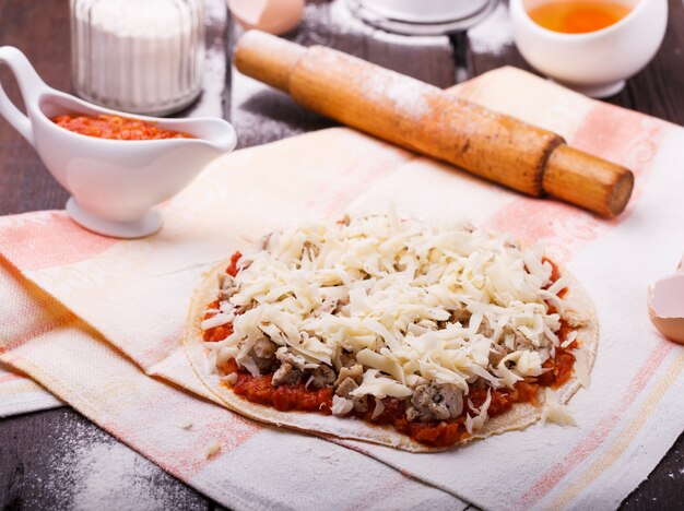 Preparação de pizza rodeada por ingredientes.